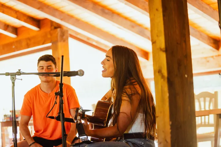 Concierto acústico bajo el porche de madera: un chico y una chica cantan con guitarra