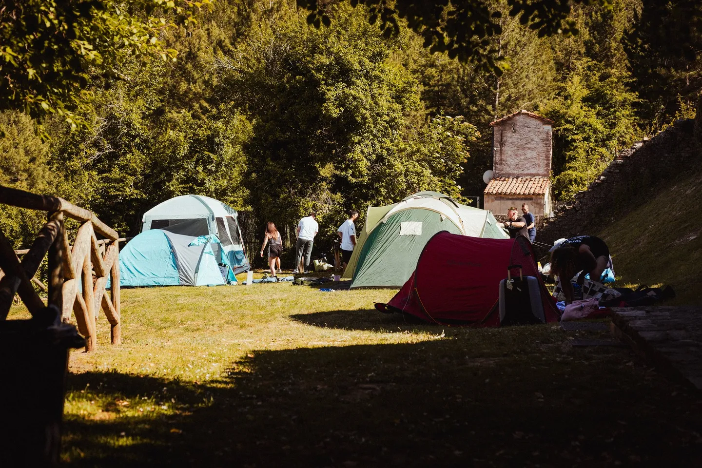 Tiendas de campaña en el camping del pueblo, a la sombra de los árboles y junto a las casas de piedra