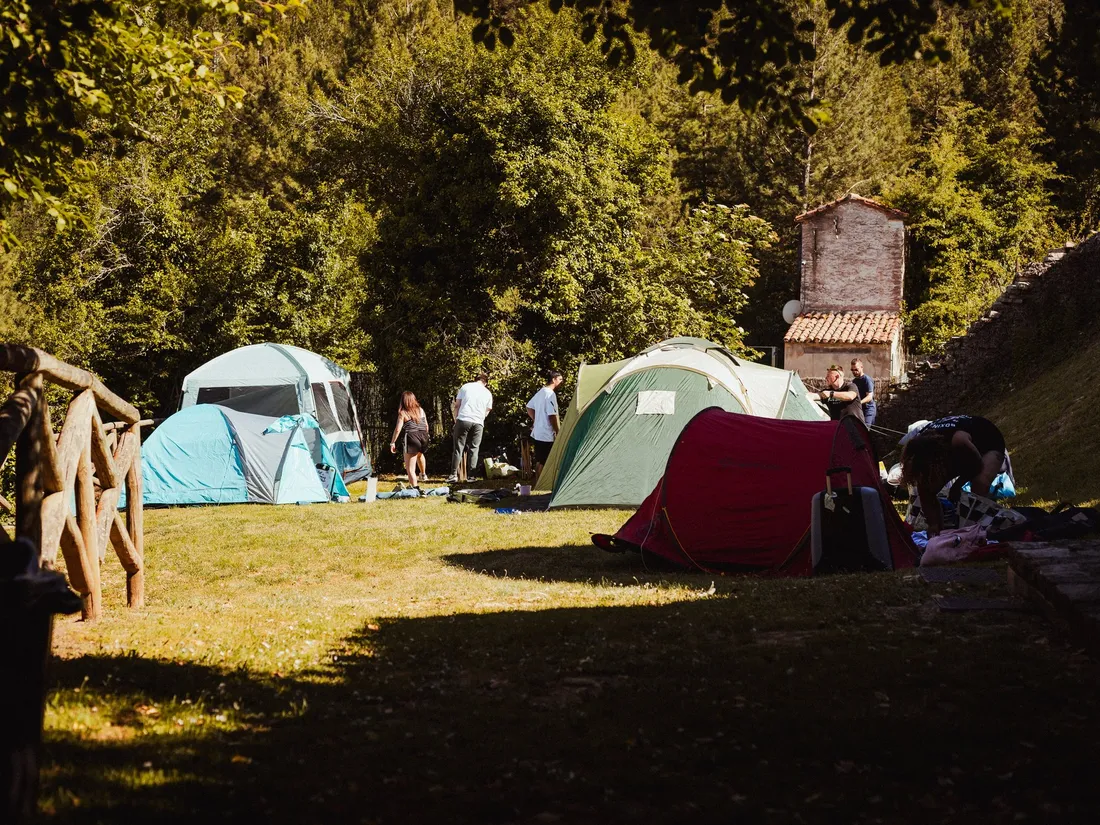Tiendas de campaña montadas en la pradera del camping, a la sombra de los árboles y junto a las casas de piedra