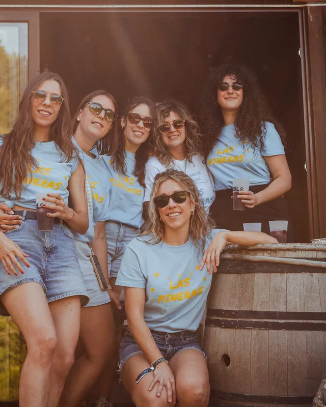 Cinco amigas con camisetas de PUEBLO toman algo en el porche de madera