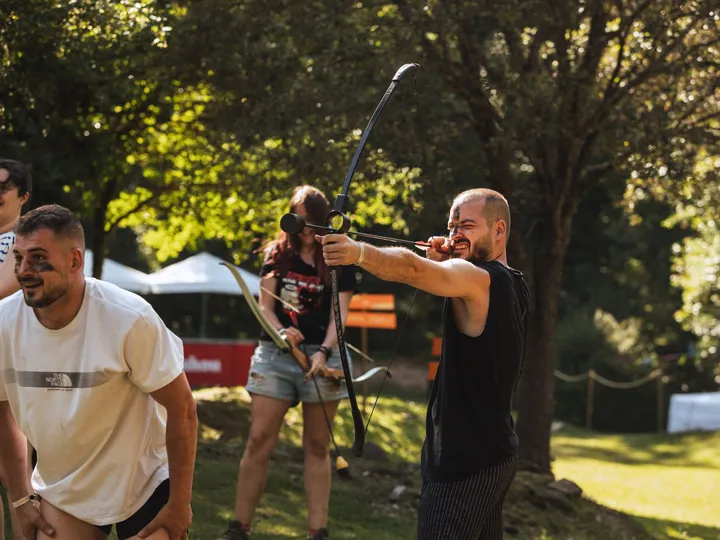 Archery tag en el bosque: un chico apunta con el arco mientras otros esquivan