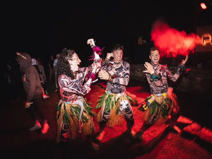 Tres personas bailan con faldas de rafia en la fiesta tropical bajo luz roja