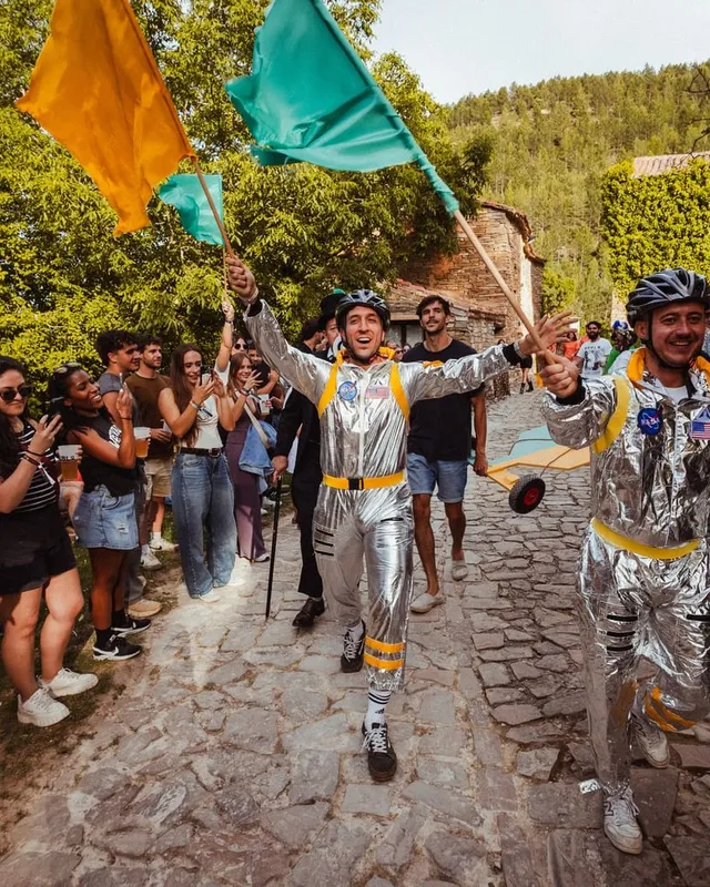 El desfile de astronautas baja por la calle empedrada entre el público y las banderas