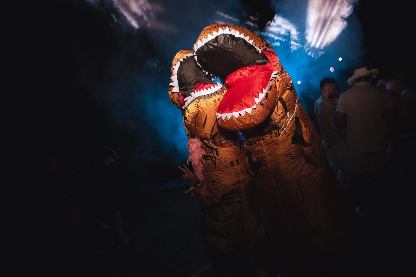 Dos disfraces hinchables de dinosaurio se «besan» en la pista entre el humo y los focos azules