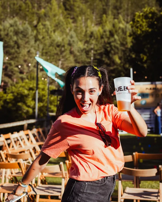 Una chica con camiseta naranja saca la lengua y levanta su vaso en la plaza, a pleno sol