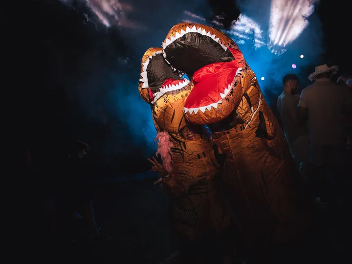 Un disfraz de dinosaurio hinchable entre las luces azules de la pista