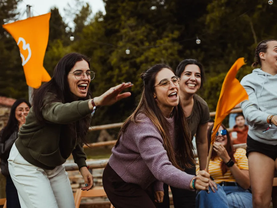 Unas amigas animan a gritos con banderines naranjas de la llama en la plaza