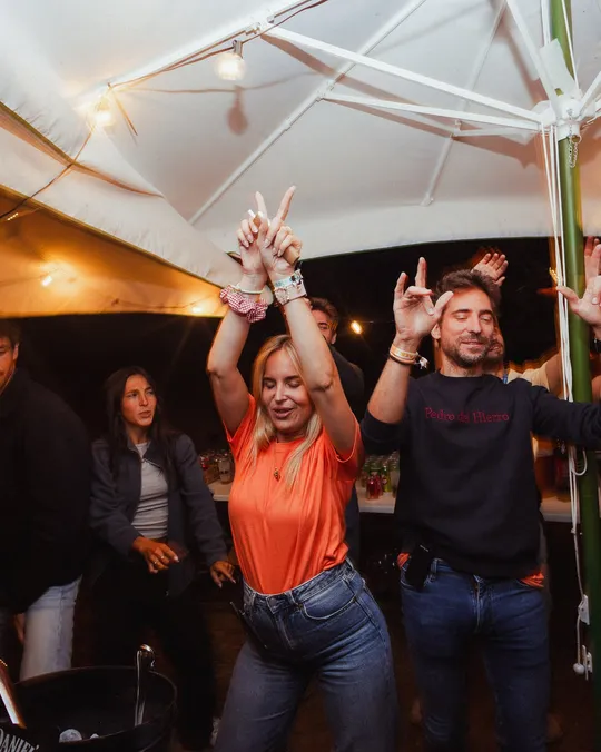 Gente bailando con los brazos en alto bajo la carpa en la fiesta del sábado