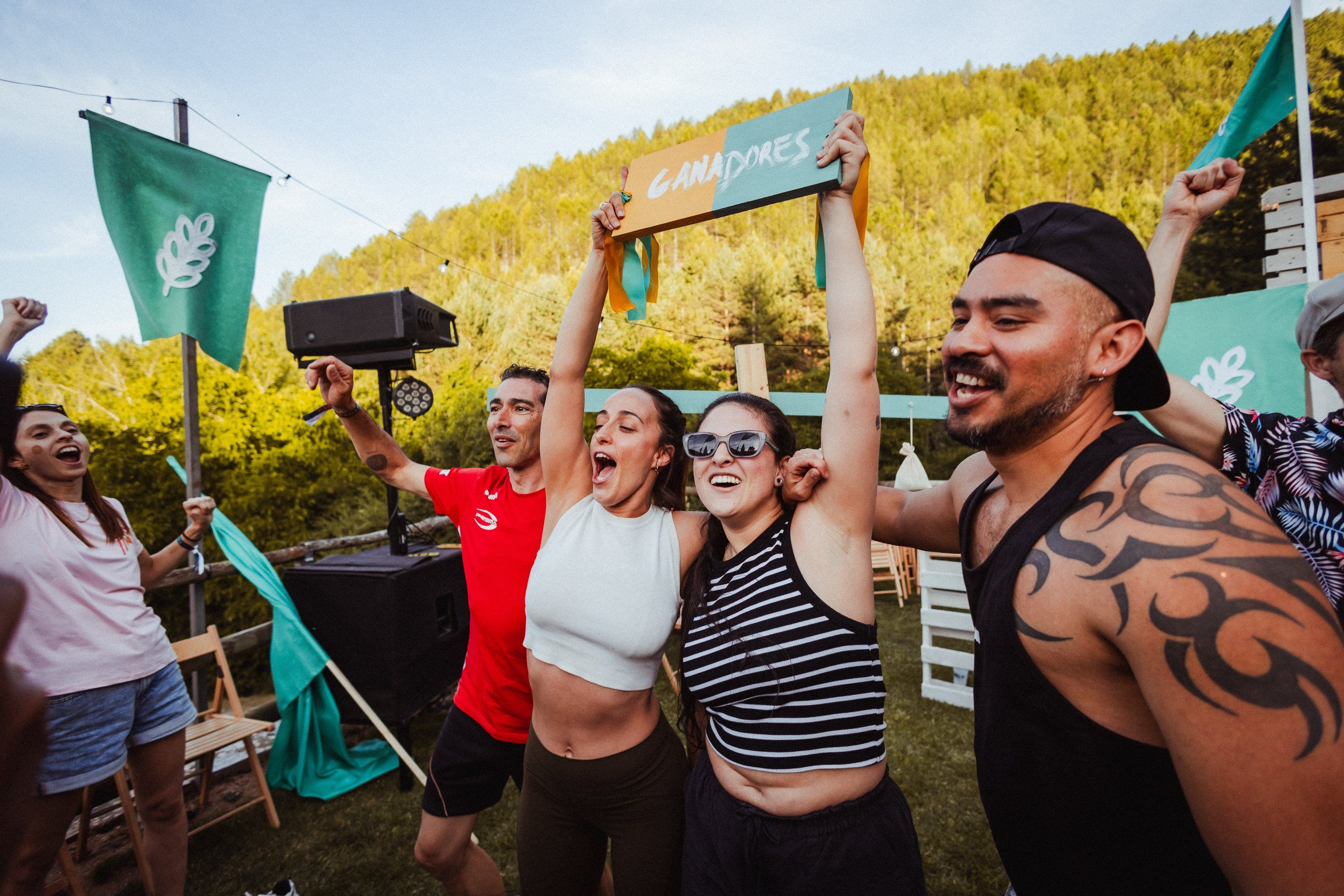 La familia ganadora celebra con los brazos en alto y el cartel «Ganadores» bajo las banderas turquesa