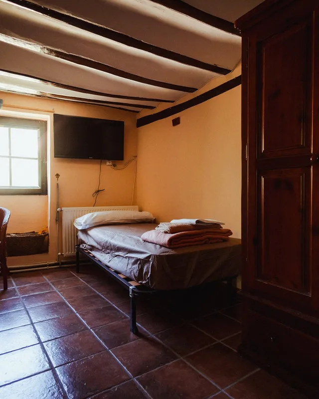 Habitación individual de una casa del pueblo con vigas de madera, armario antiguo y ventana con cortinas