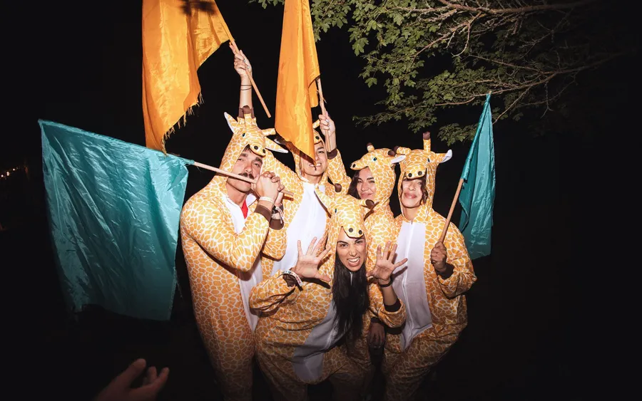 Un grupo disfrazado de jirafa con banderas turquesa y naranja en una fiesta de PUEBLO 2025