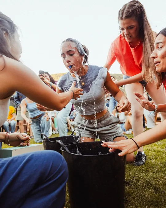 Prueba de las cubetas: una chica mete la cabeza en un cubo de agua mientras su equipo la anima