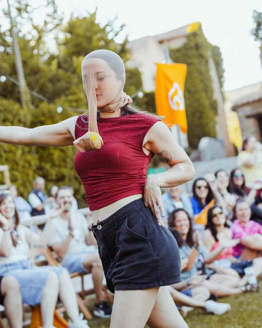 Una participante con una media en la cabeza balancea una pelota delante del público