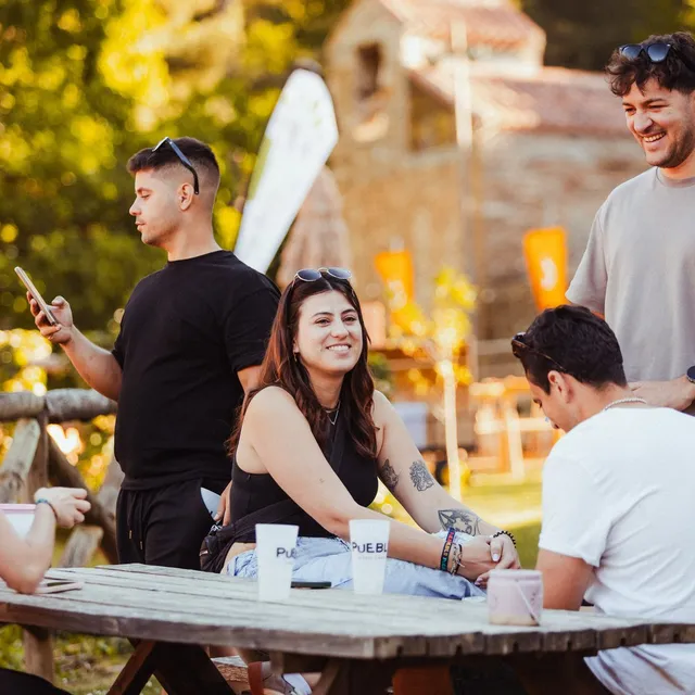 Amigos recién llegados ríen alrededor de una mesa de madera al sol