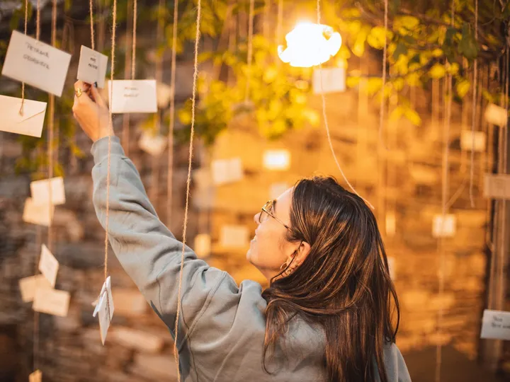 Una chica cuelga una nota en el muro de mensajes bajo las luces cálidas