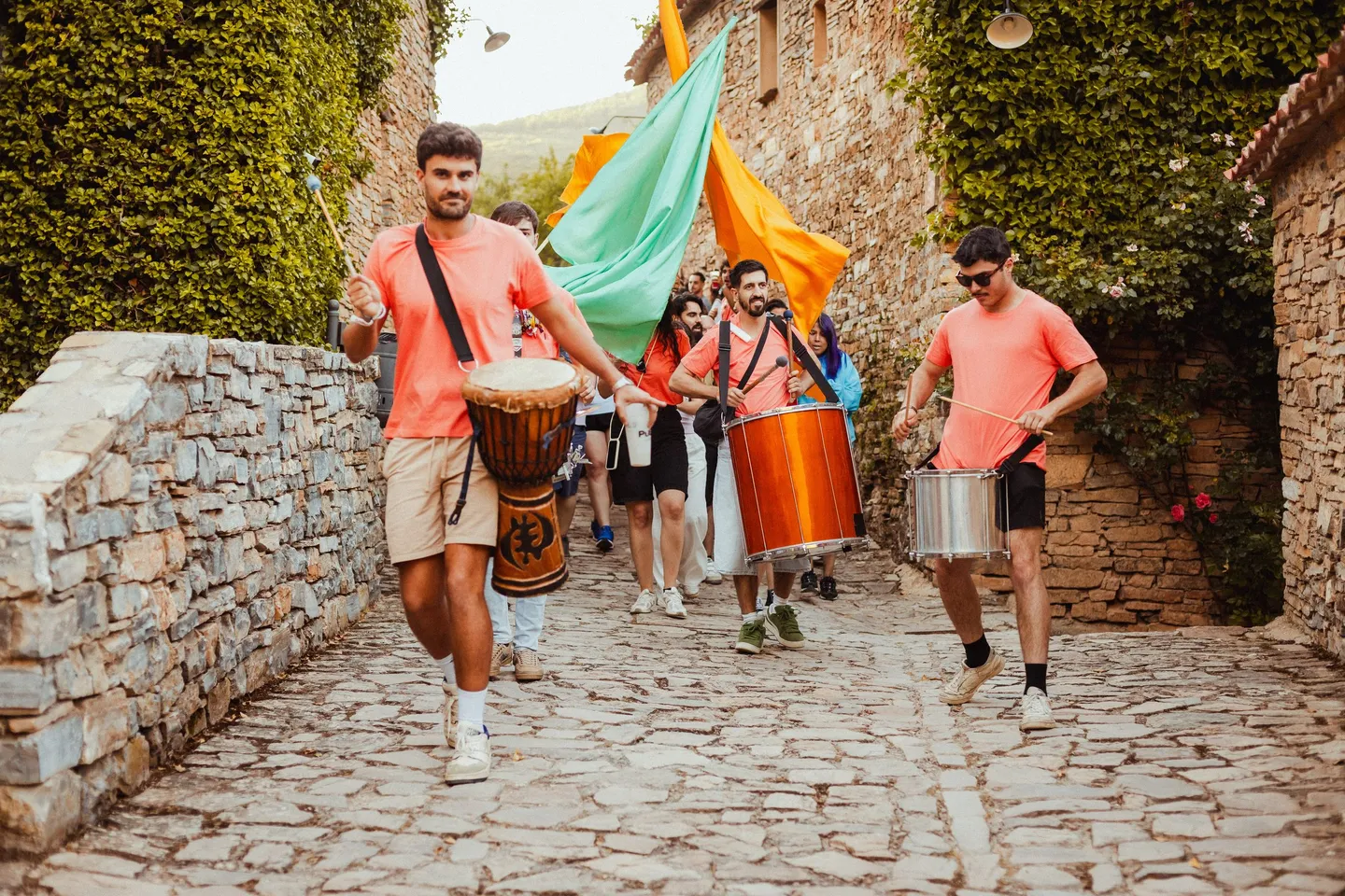 La charanga de PUEBLO Fest Camp baja por una calle de piedra de Valdelavilla con banderas y tambores