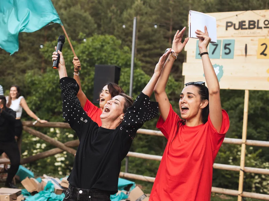 Dos monitoras celebran con los brazos en alto y una bandera turquesa junto al marcador de puntos