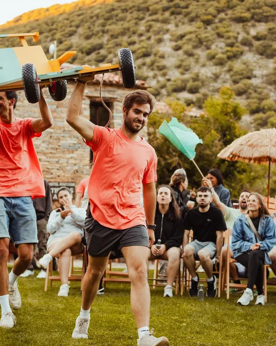 Dos chicos cargan un carro de madera sobre la cabeza en la gran final, ante el público sentado