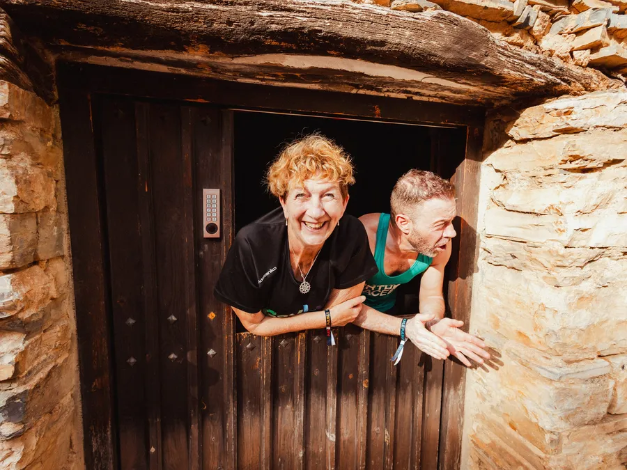 Dos personas asomadas, sonrientes, a una ventana de madera de Valdelavilla